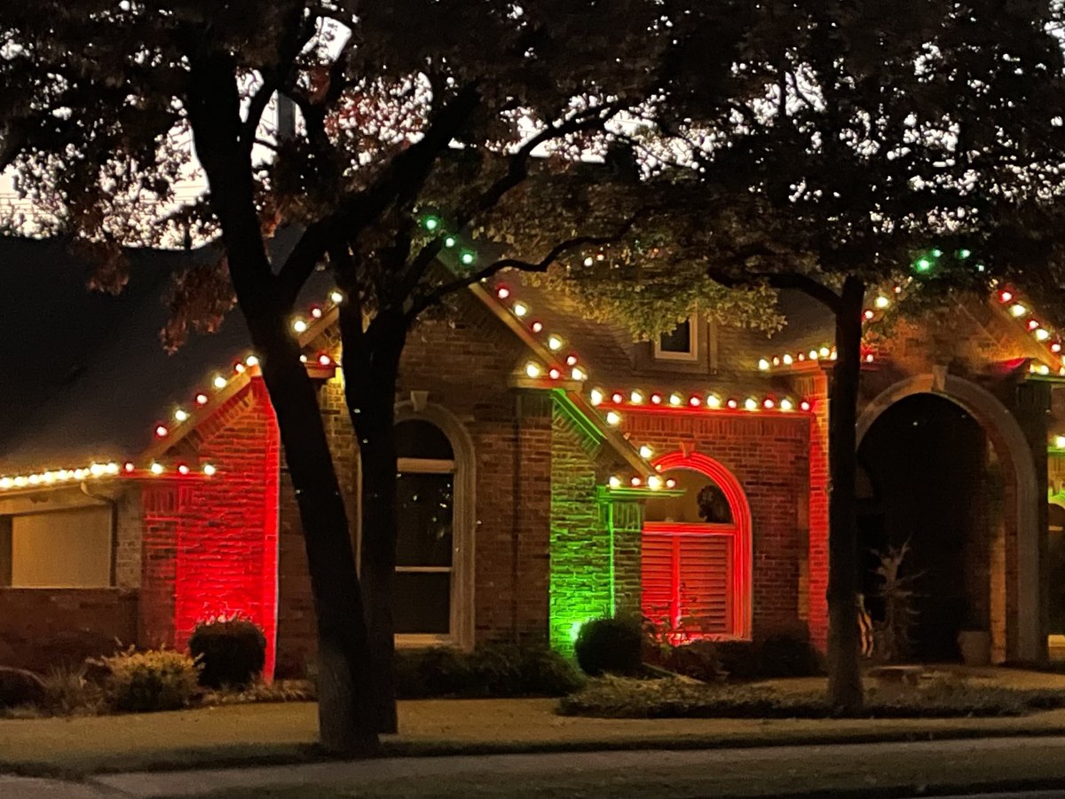 Brick home with warm white roofline lights and red and green uplighting across the front elevation and entry arch
